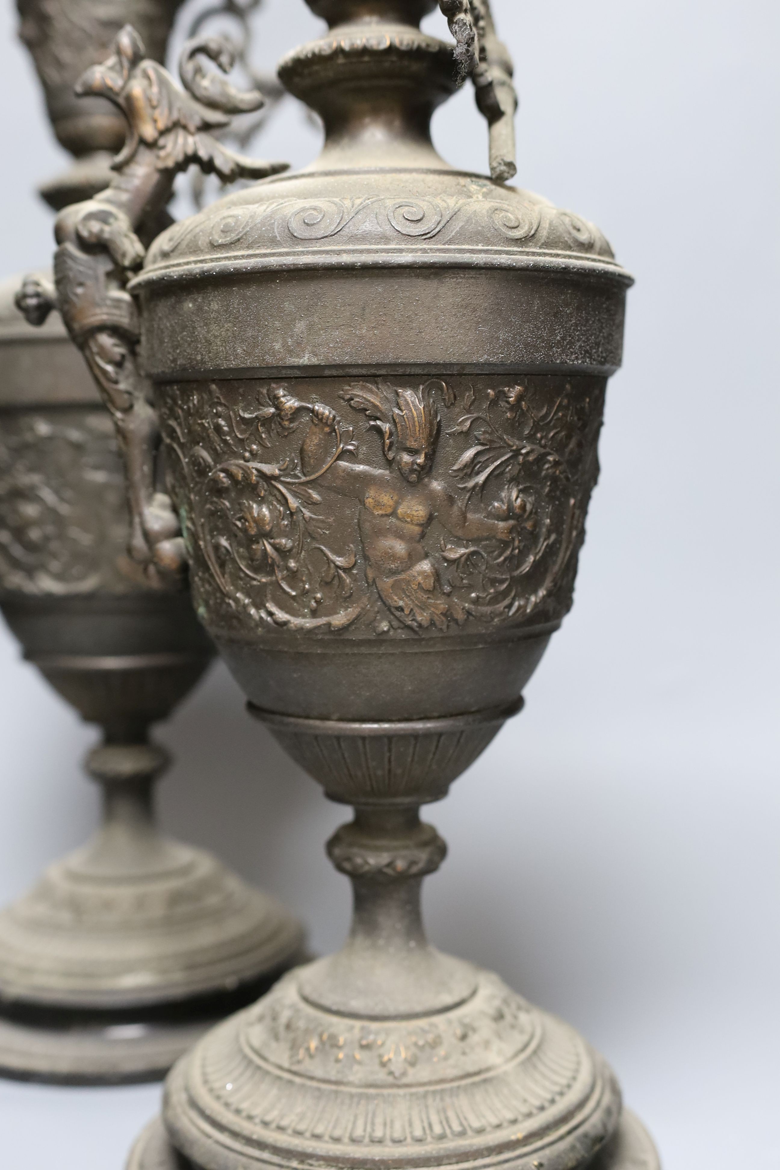 A pair of bronzed metal classical pedestal urns with scroll decoration and satyr masks (one handle detached), height 53cm